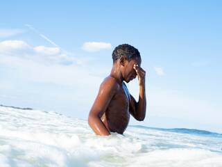 A man waist deep in the ocean covering his eyes